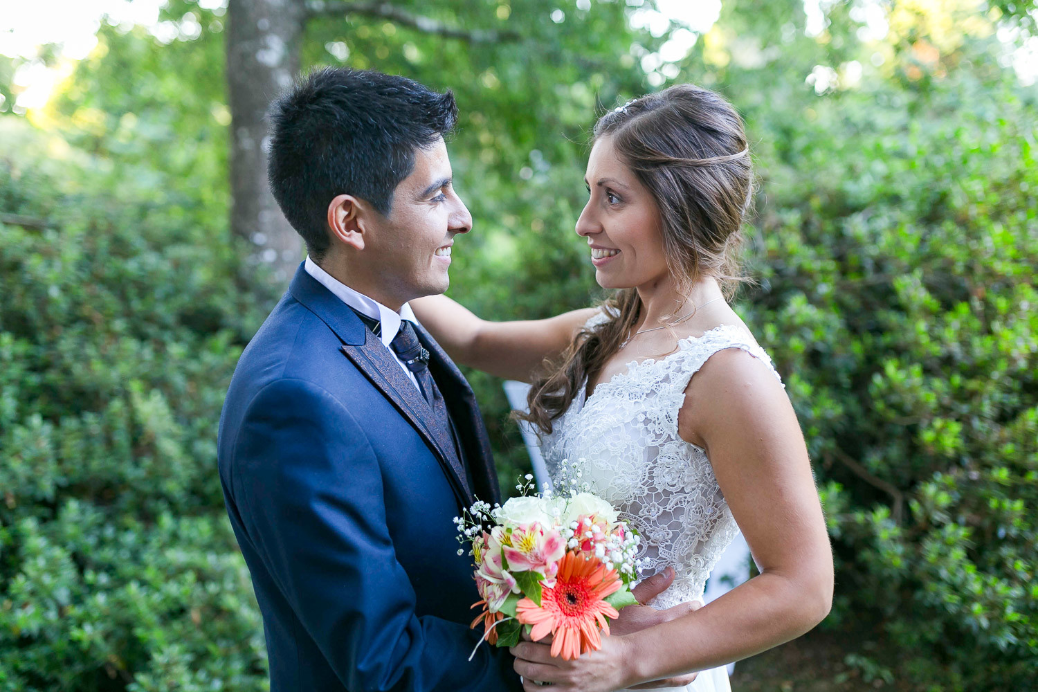 pareja de novios en el dia de su boda el hombre vistiendo un traje de novio color azul marino y la mujer con vestido de novia blanco y ramo de flores en manos