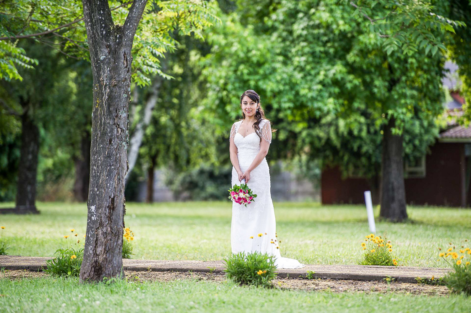 mujer joven con Vestido de novia tropeta con escote semi corazón blanco y rama de flores rosas en la mano al aire libre con vegetación y naturaleza al rededor en chile en el día de su casamiento