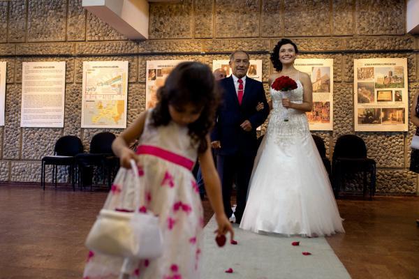 Novia con su padre y en el ensayo para el matrimonio la novia lleva puesto un vestido de novia bordado a mano y un ramo de tirar de rosas rojas