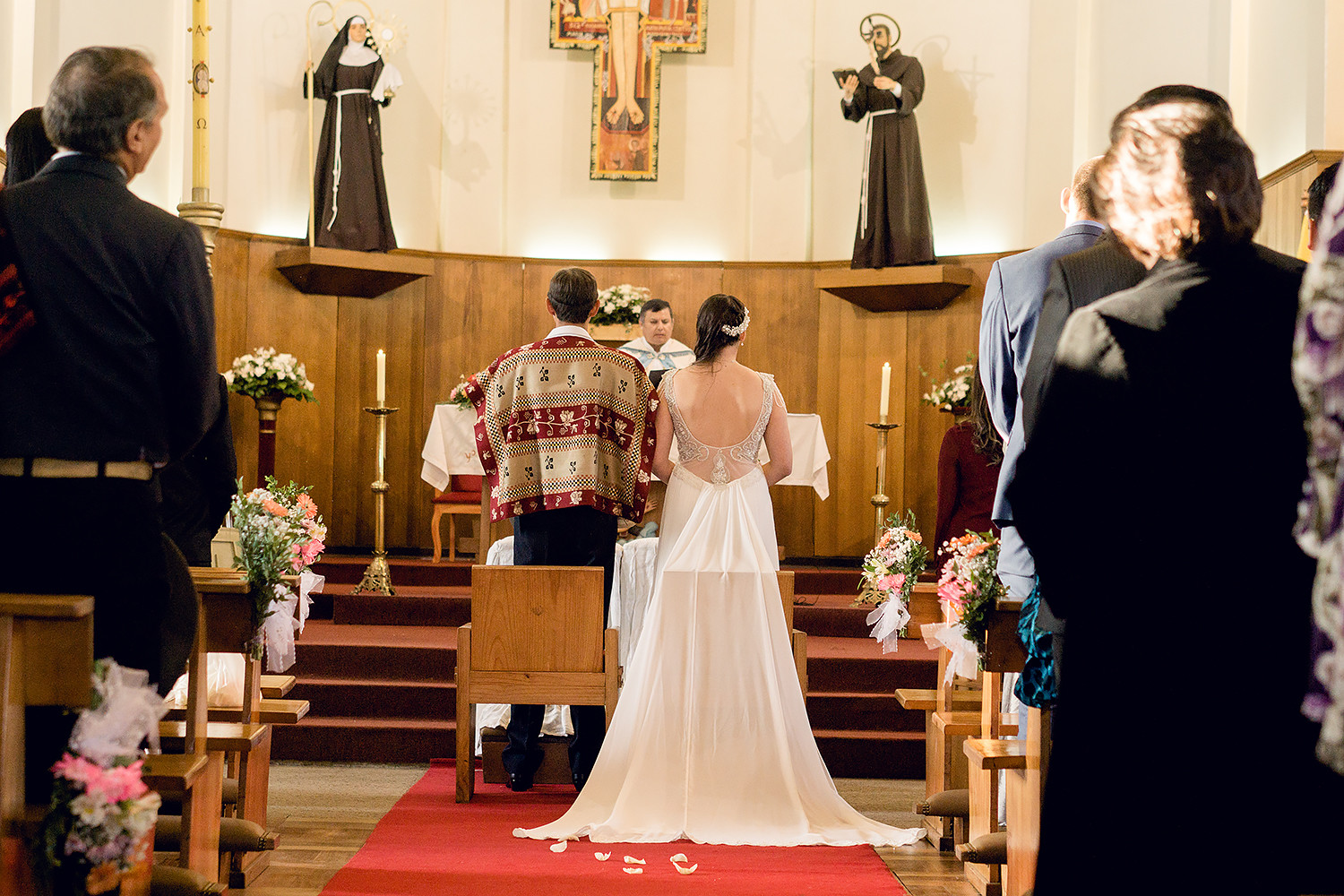 pareja de novios en casamiento tradicional chileno en la iglesia, el novio lleva una tradicional ropa de huaso y la novia un vestido imperio con espalda escotada y cola de chiffon