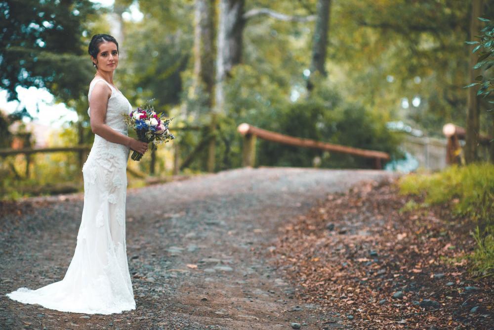 novia en bosque verde sur de chile con vestido blanco con cola y rama de tirar posando para foto oficial de su boda